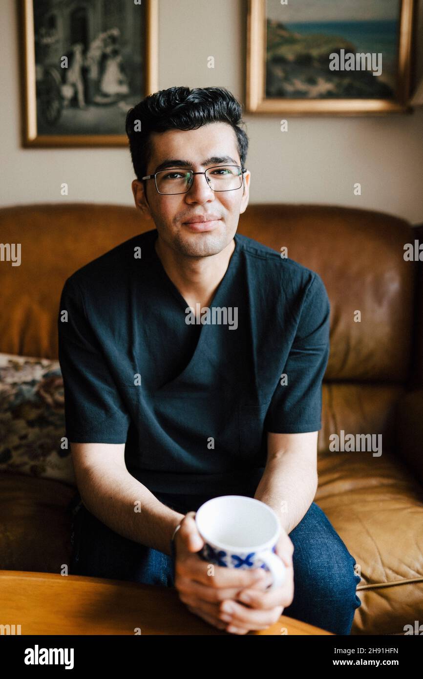 Ritratto di uomo sorridente con tazza di caffè in salotto a casa Foto Stock