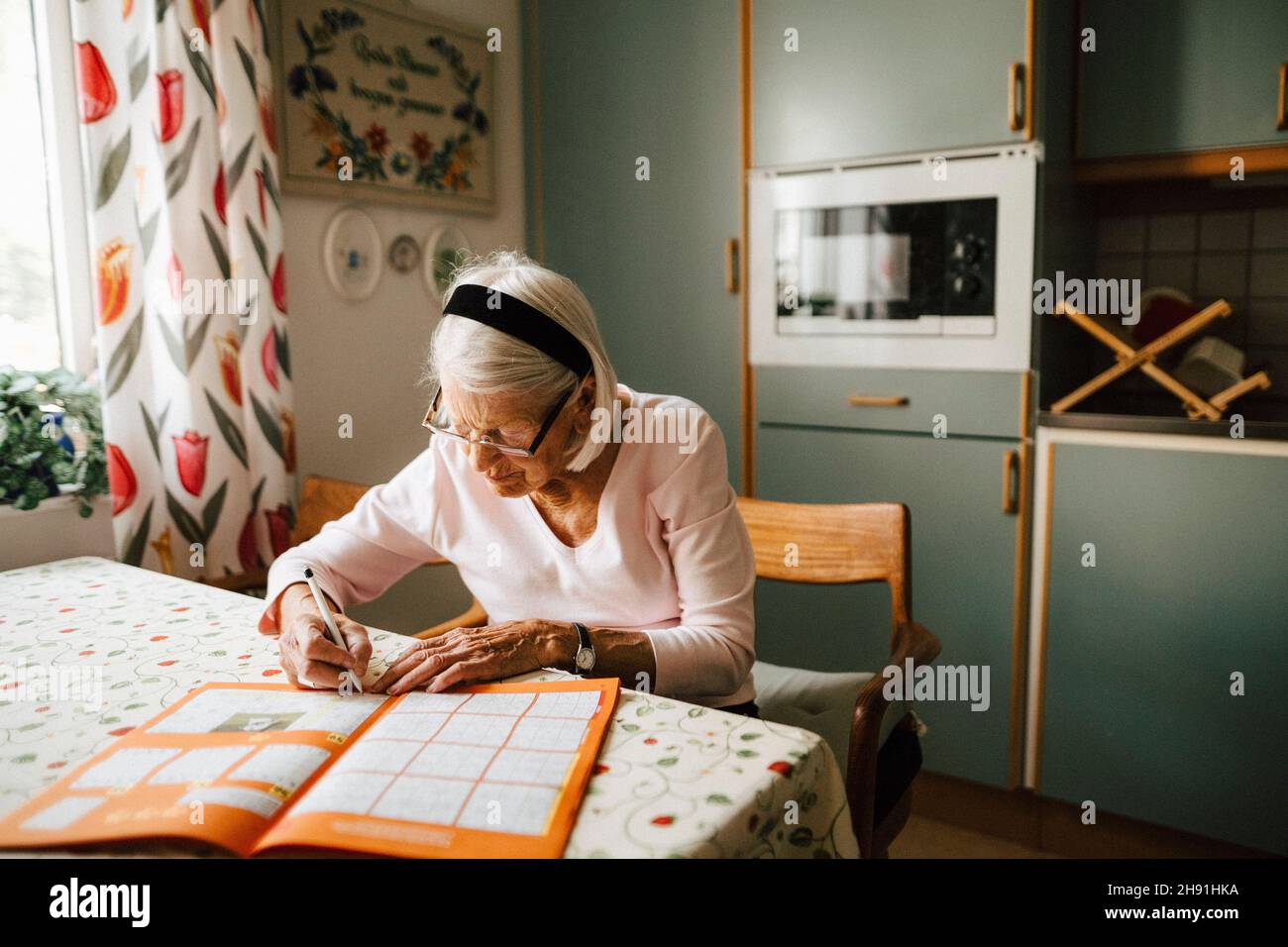 Donna anziana che risolve sudoku al tavolo da pranzo in cucina Foto Stock