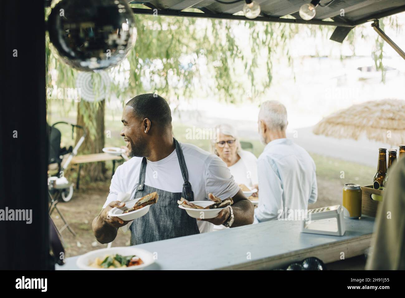 Sorridente proprietario maschio con ordine di clienti al banco del camion alimentare Foto Stock