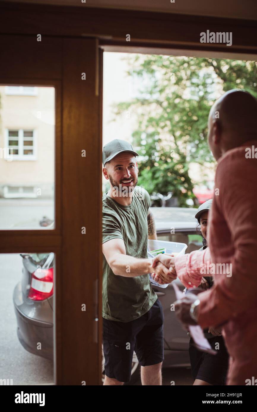 Uomo maturo che fa una stretta di mano con un tecnico maschio alla porta Foto Stock