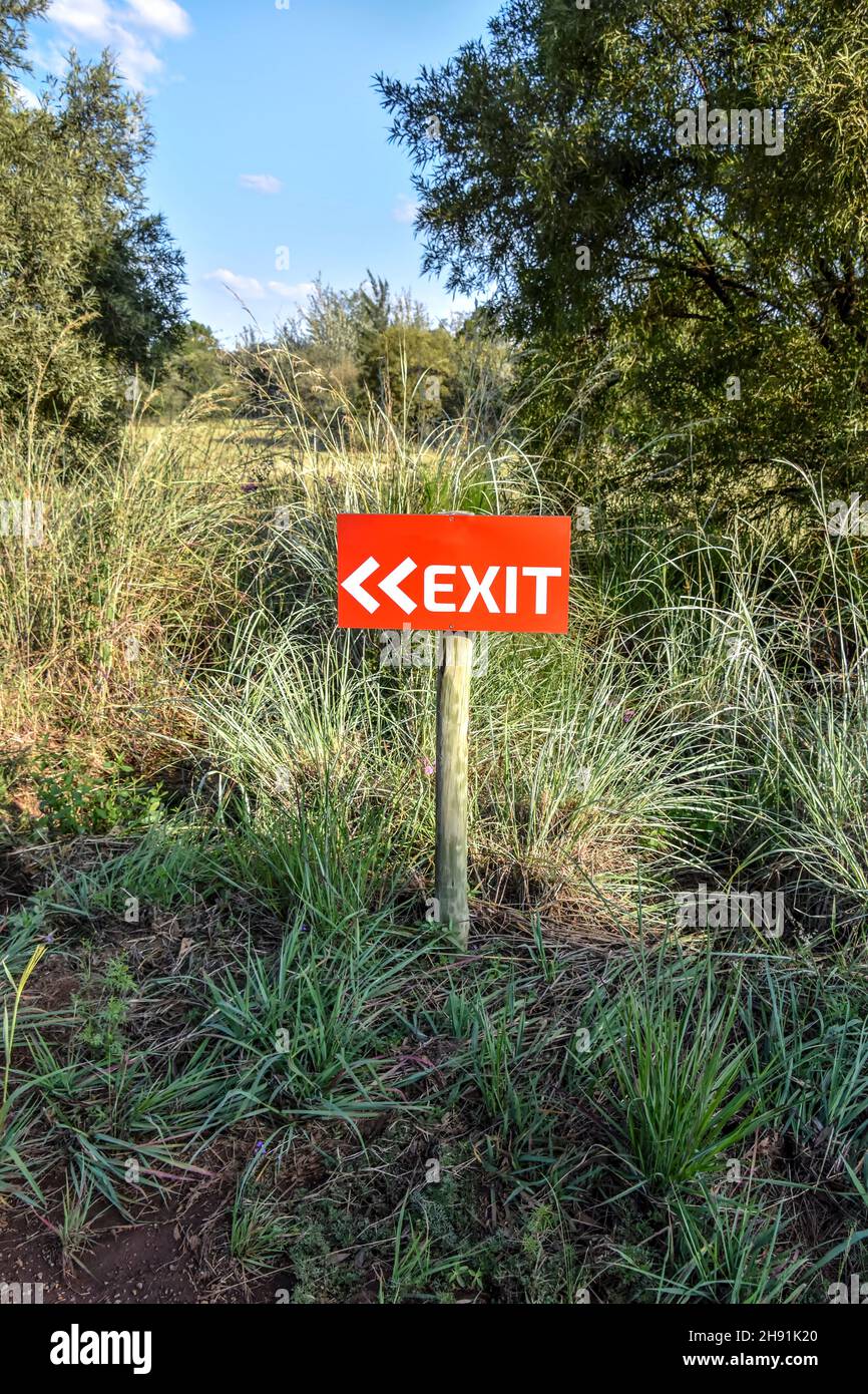 Un cartello di uscita bianco e rosso che punta a sinistra in erba alta vicino agli alberi con frecce su un palo di legno che fornisce la direzione ai viaggiatori Foto Stock