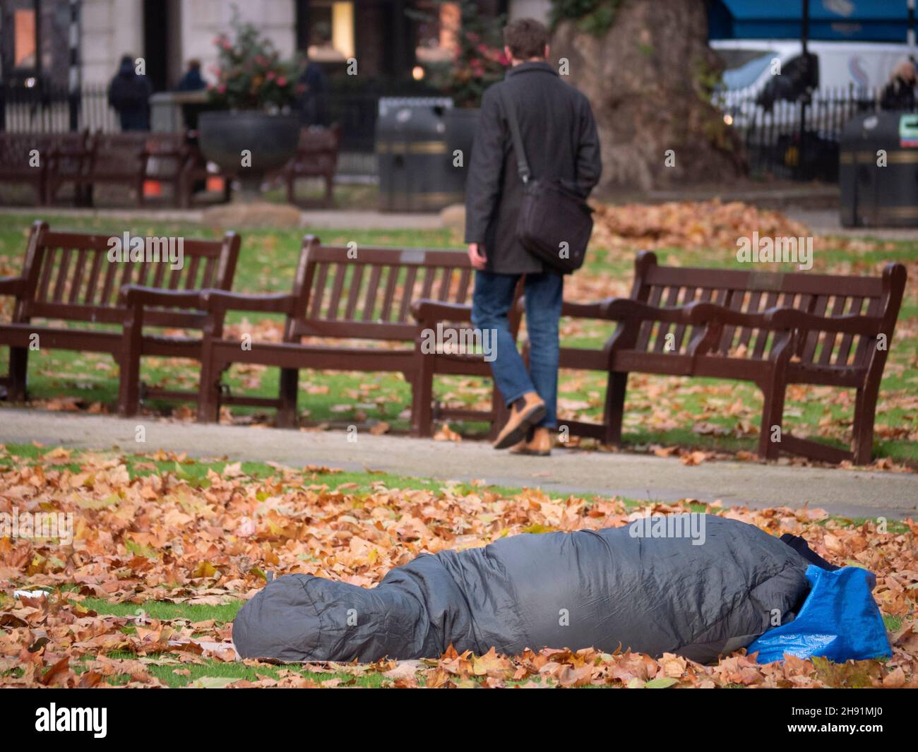 I ricchi poveri dividono la disuguaglianza, i senzatetto che dormono a Berkeley Square Mayfair tra le foglie autunnali in condizioni di congelamento mentre i lavoratori del collare bianco degli uffici camminano Foto Stock