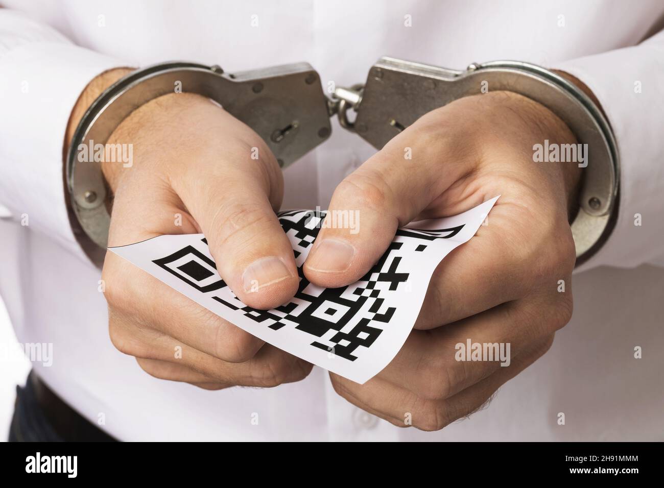 Un uomo in manette tiene un foglio con un codice a barre, il concetto di punizione per la falsificazione dei codici QR Foto Stock