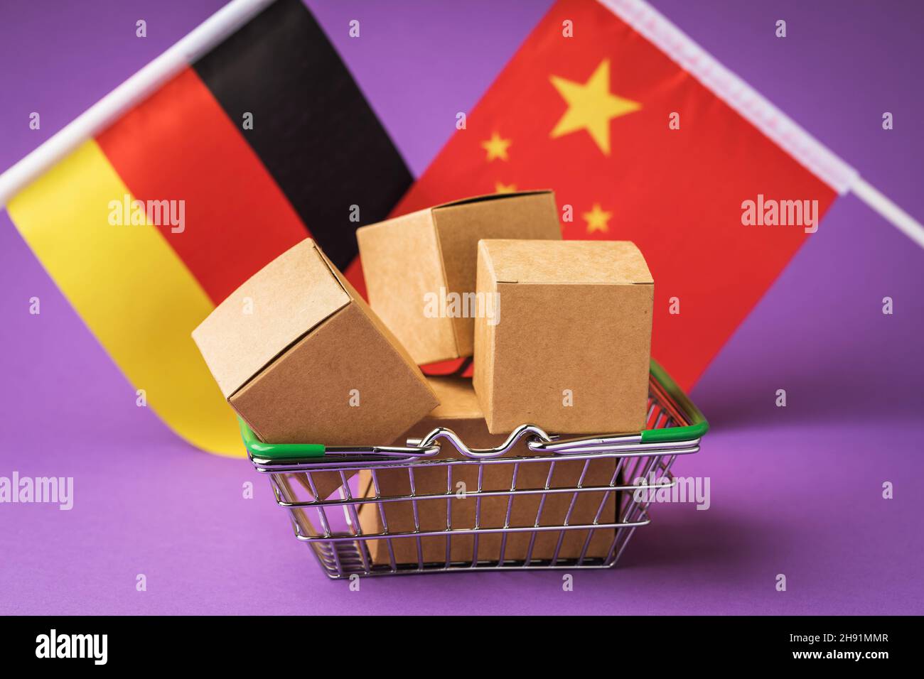 Scatole di cartone in un cestino alimentare e bandiere di Cina e Germania su uno sfondo colorato, il concetto di commercio tra paesi Foto Stock