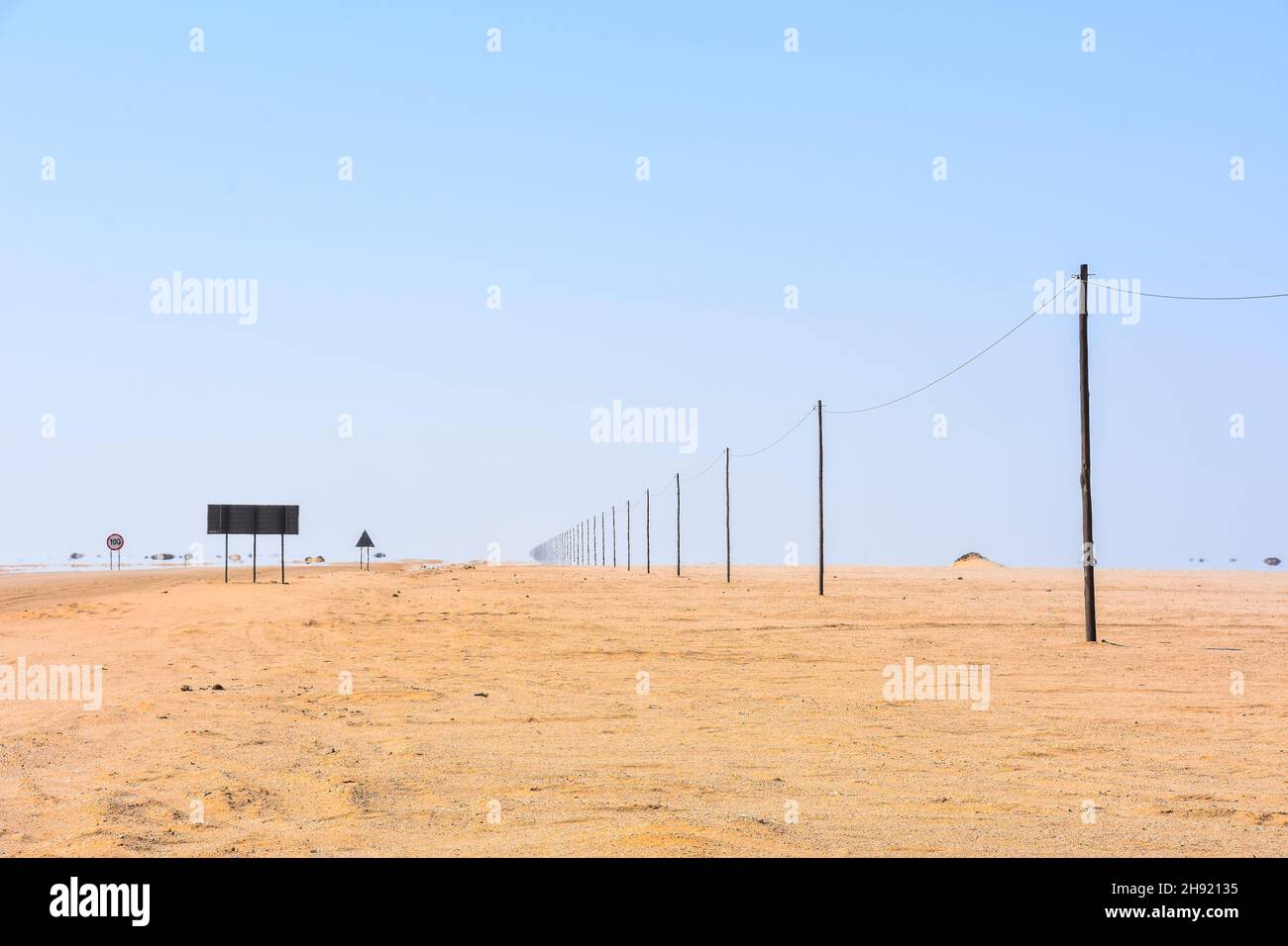 Una lunga fila di pali di legno e un electricy o cavo telecom in Namibia in Africa australe vicino a una strada nel deserto in fuga la distanza con un miraggio ef Foto Stock