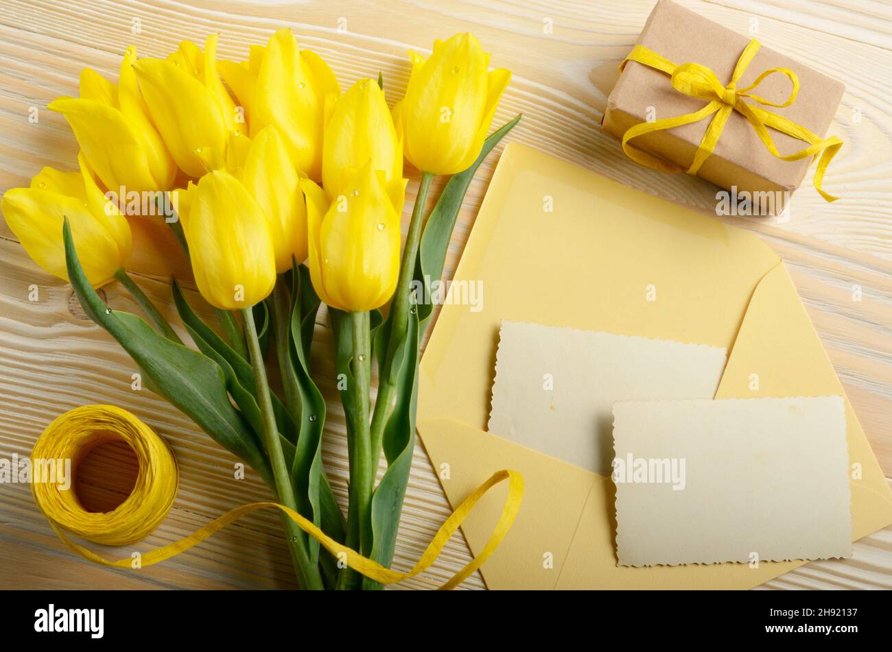 Tulipani gialli vicino bigliettino vuoto confezione regalo e una busta sul legno naturale sfondo con spazio per il testo Foto Stock