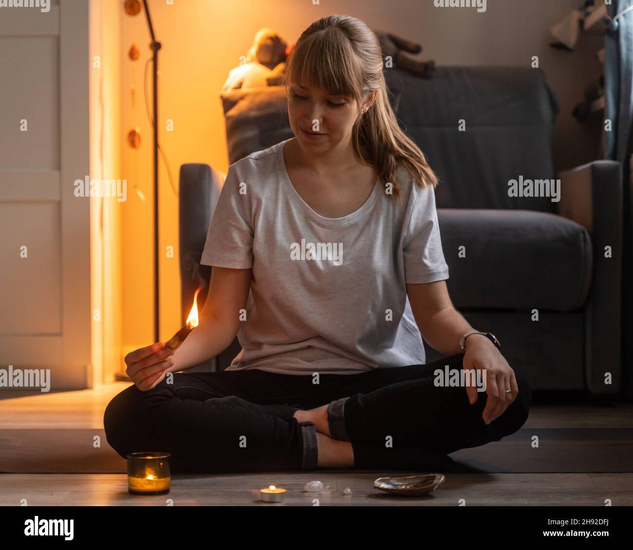 Donna che tiene il bastone aromatico di saldanwood mentre meditating in serata accogliente a casa Foto Stock
