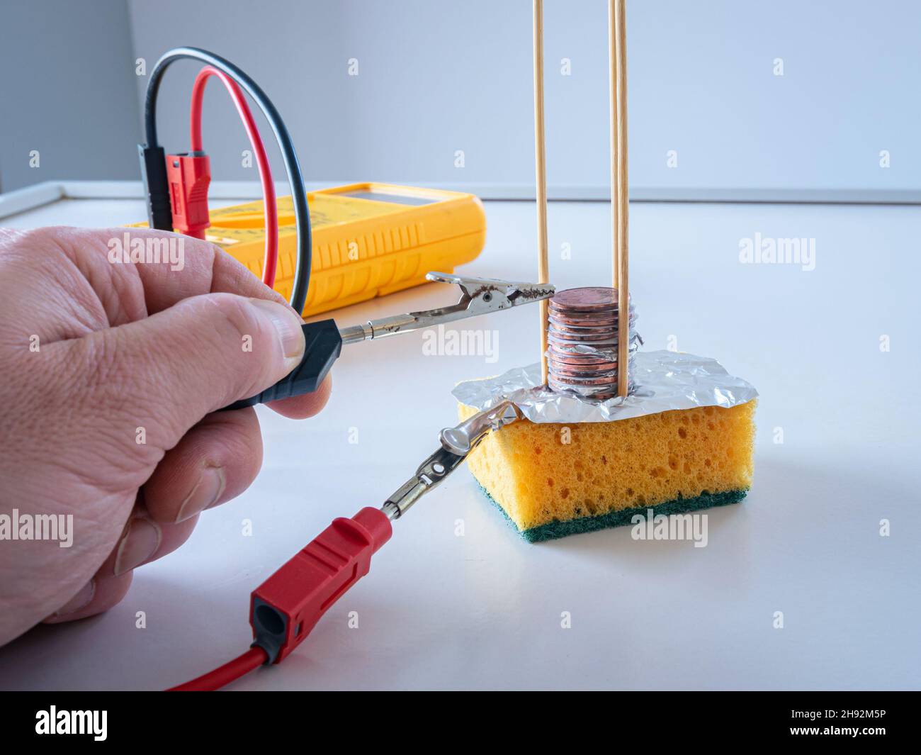 Misurare la tensione elettrica sul palo di volta fatto da una pila di monete di rame, carta da filtro in acqua salata e lamina di alluminio. Foto Stock