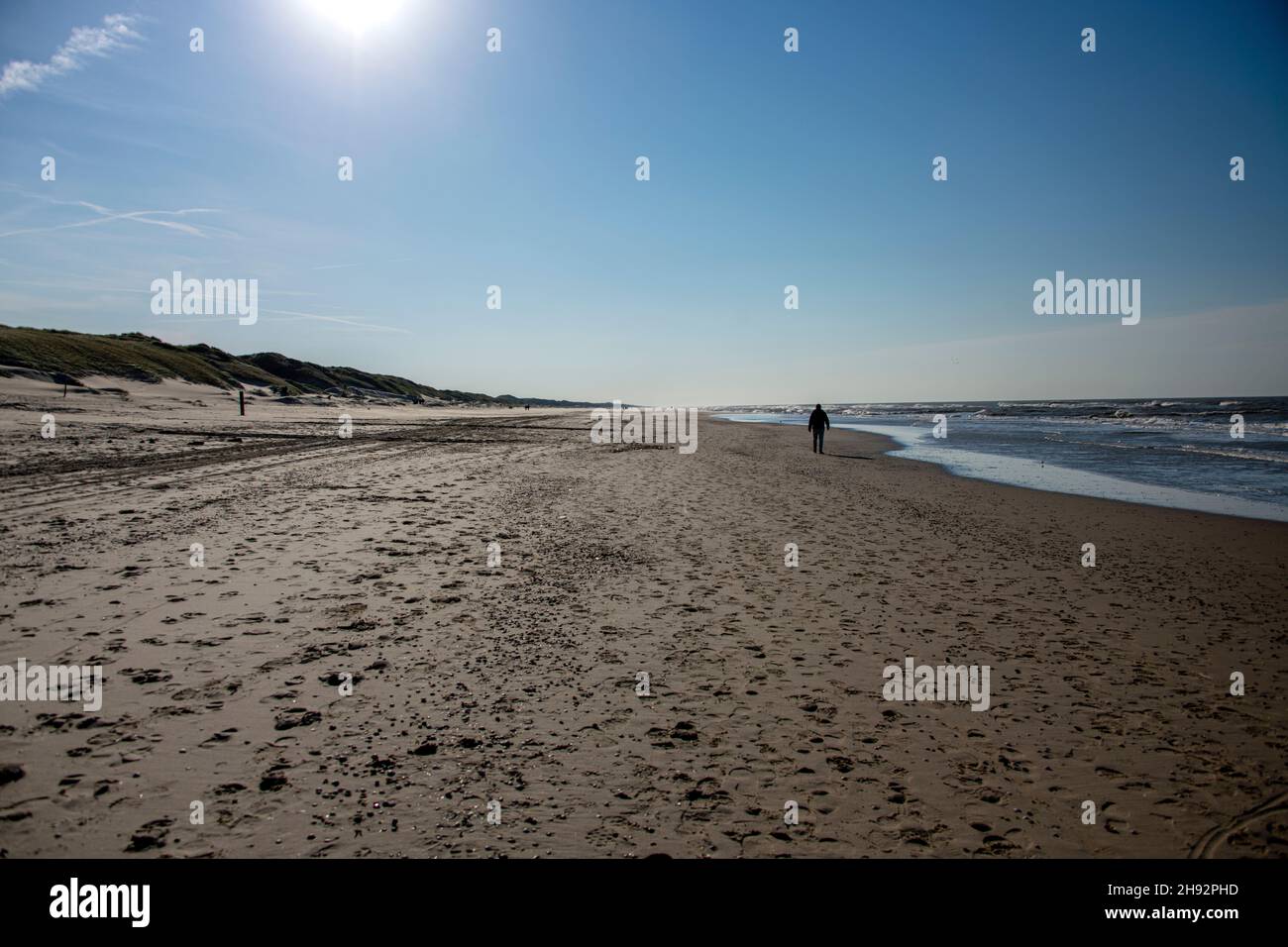 Uomo solo camminando sulla spiaggia tra le onde del mare e le dune di sabbia in una giornata di sole Foto Stock