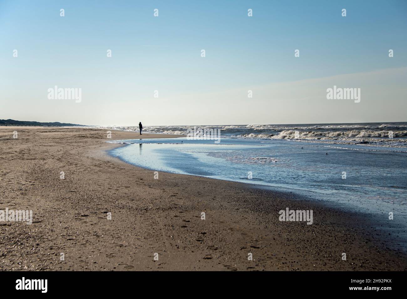 Uomo solo camminando sulla spiaggia tra le onde del mare e le dune di sabbia in una giornata di sole Foto Stock