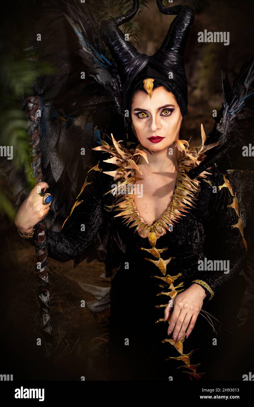 MALEFICENT COSPLAY. RITRATTO, CARATTERE SCURO CON CORNA AFFILATE E ALI FORTI. FATA MALVAGIA IN ABITO NERO. OCCHI GIALLI. VERTICALE. COLORE. Foto Stock