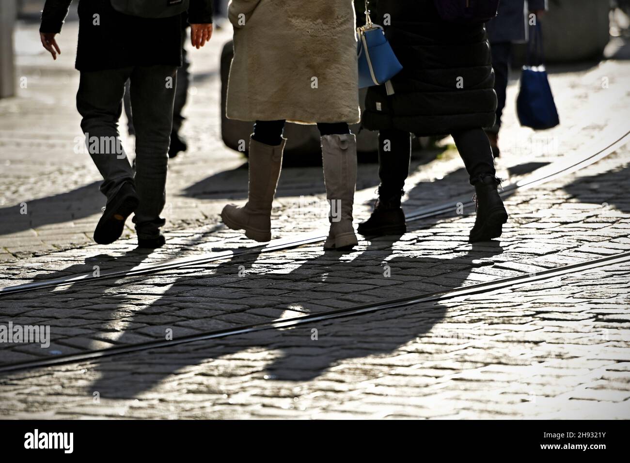 Monaco di Baviera, Germania. 03 dicembre 2021. Le persone camminano nella luce versus sopra i ciottoli e i binari del tram - gettano lunghe ombre scure sul marciapiede, accreditamento: dpa/Alamy Live News Foto Stock
