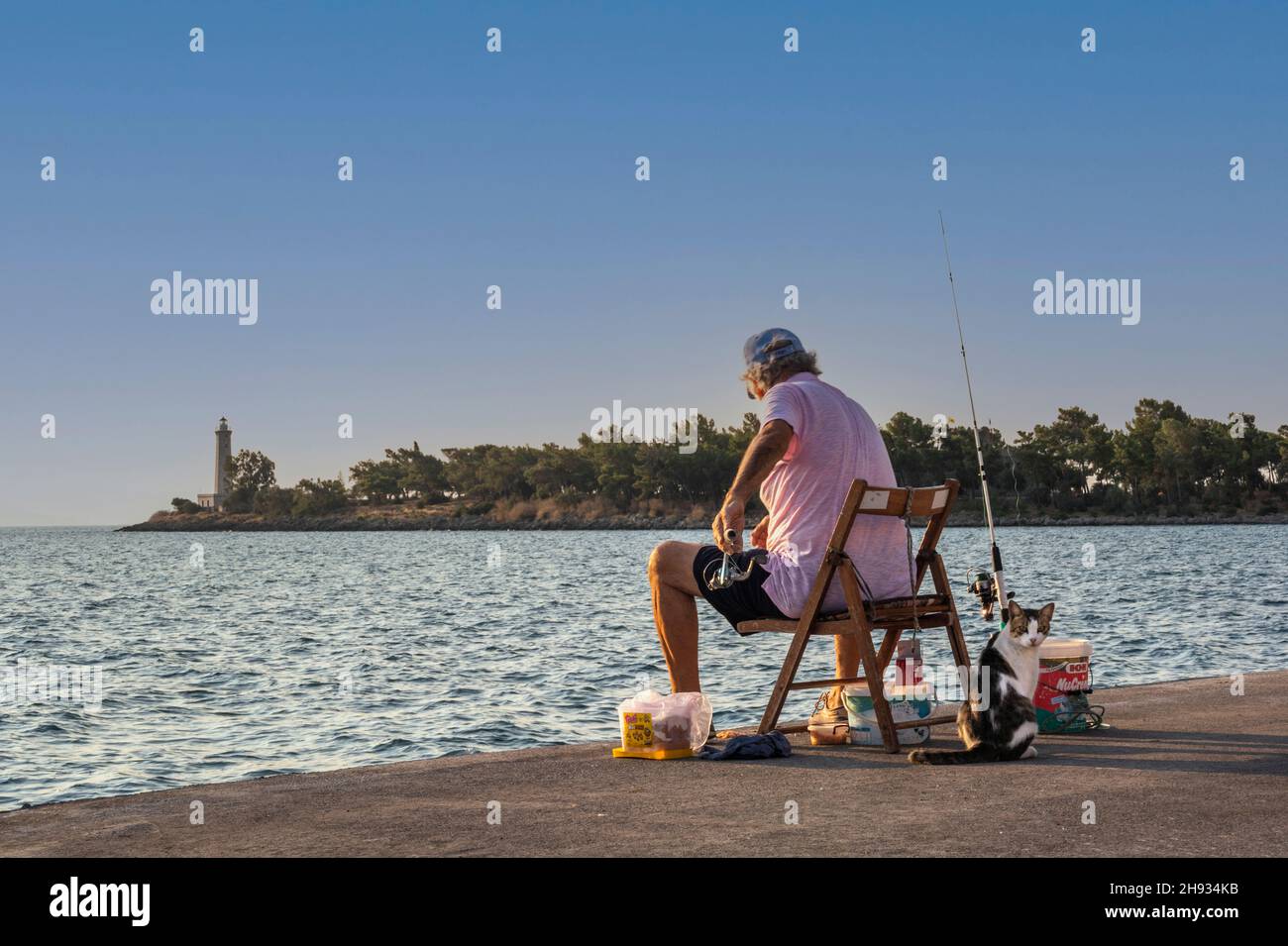 L'uomo e il suo gatto pescano nella luce del mattino presto a Gytheio, in Grecia Foto Stock