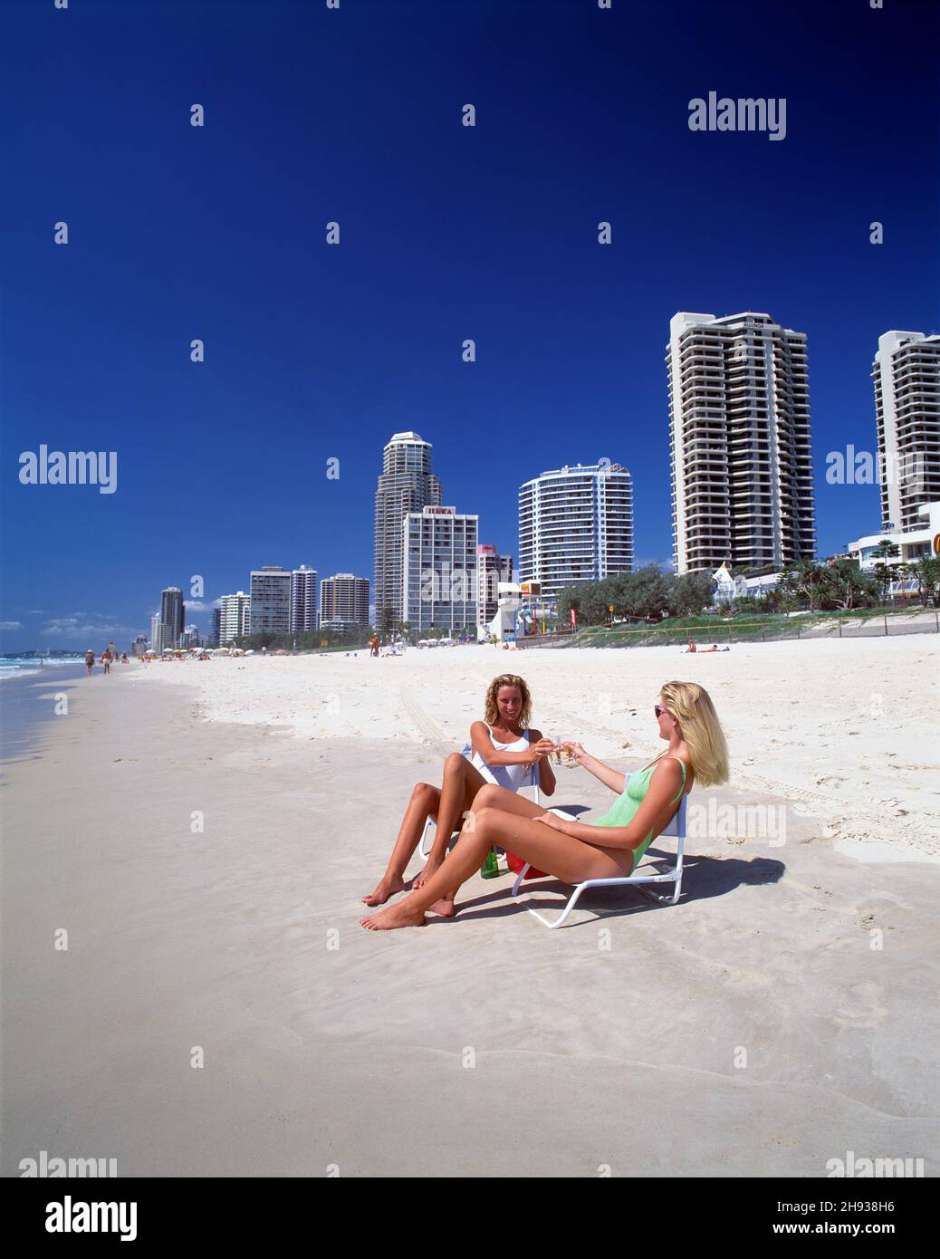 Australia. Queensland. Surfers Paradise. Due giovani donne sedute sulle sedie in spiaggia. Foto Stock
