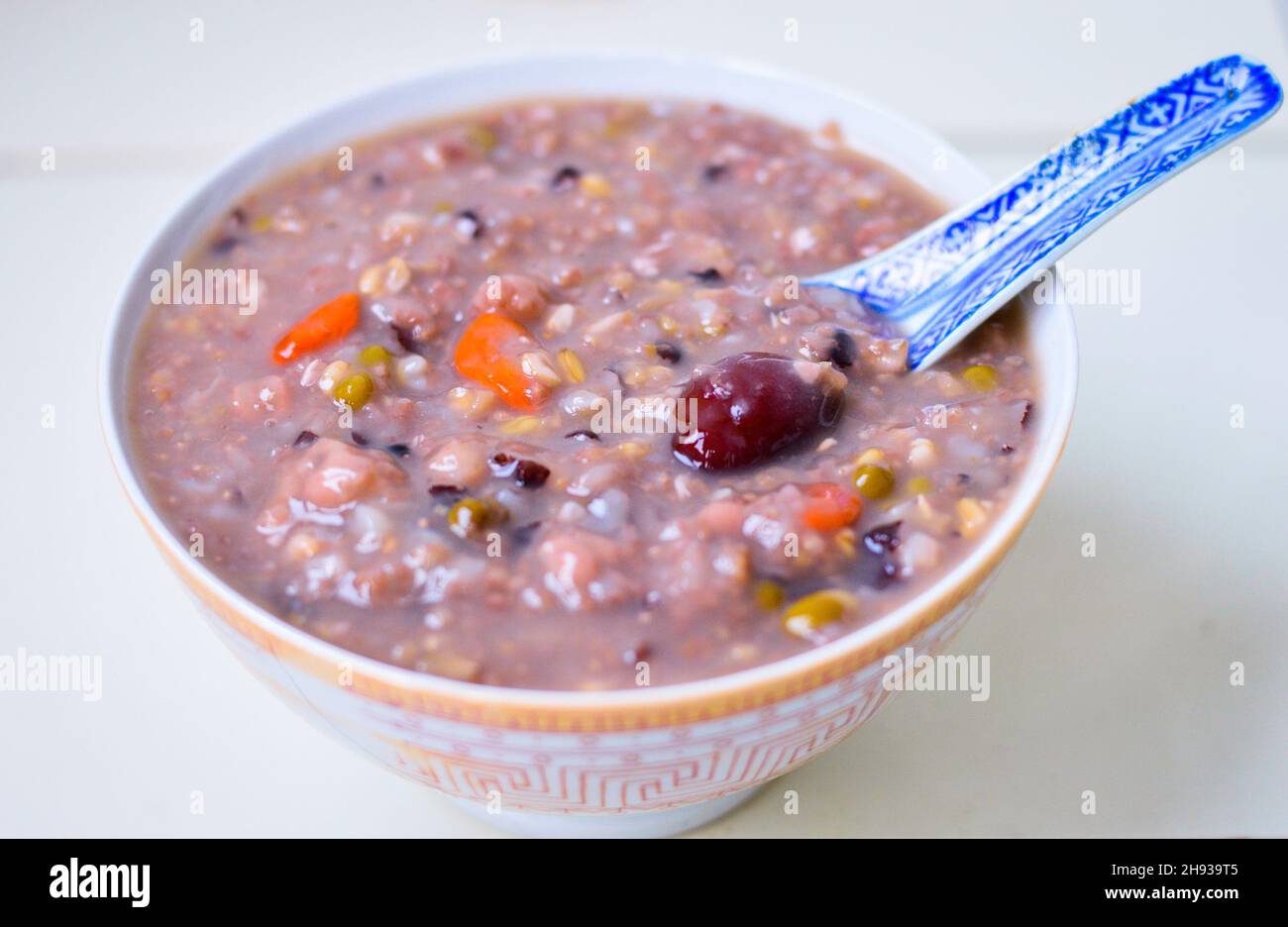 Porridge cinese sano fatto in casa multi grano in una ciotola con jujube bacca di goji sulla parte superiore e isolato su sfondo chiaro. Foto Stock