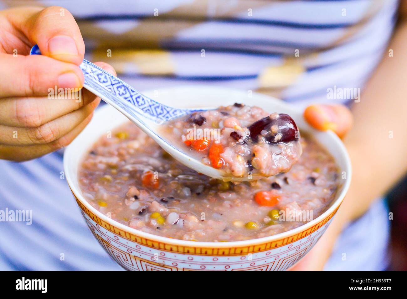 Donna mani cucchiaio su porridge multi grano da una ciotola con jujube e goji bacche sulla parte superiore. Foto Stock