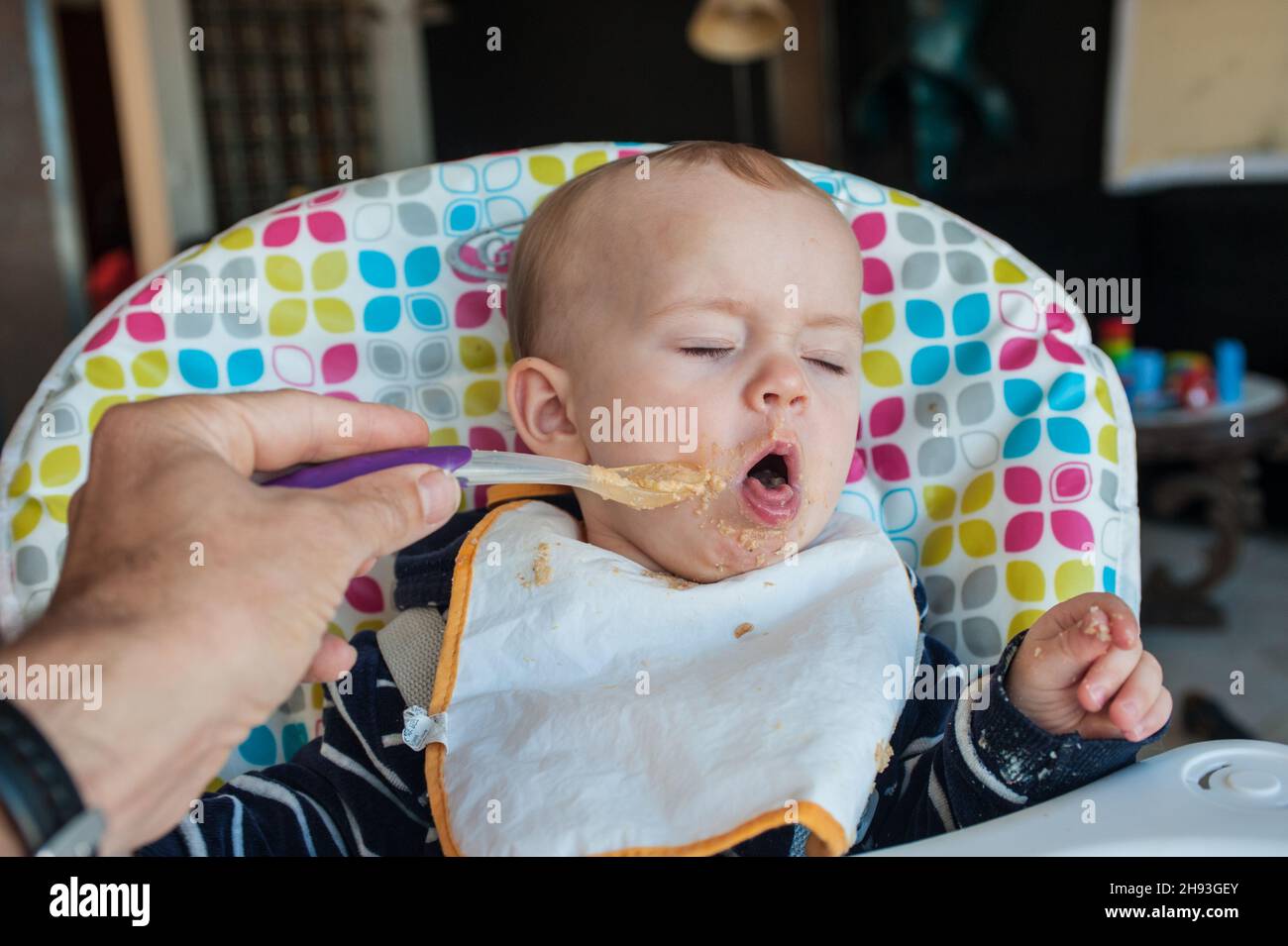 Una bambina (ca. Dieci mesi di età) viene imboccato con la sua Cena di purea di cibo e respinge un cucchiaio con una faccia disgustata. Foto Stock