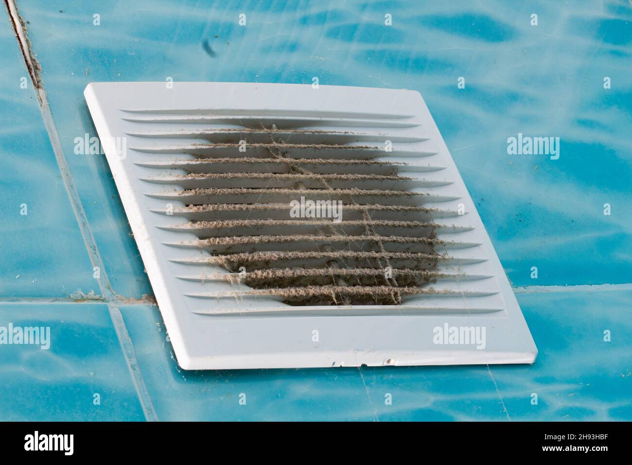 Il ventilatore del bagno era molto sporco. Ventola molto sporca con griglia in plastica bianca. Le apparecchiature elettriche devono essere pulite. Piastrelle blu con un motivo in bagno Foto Stock