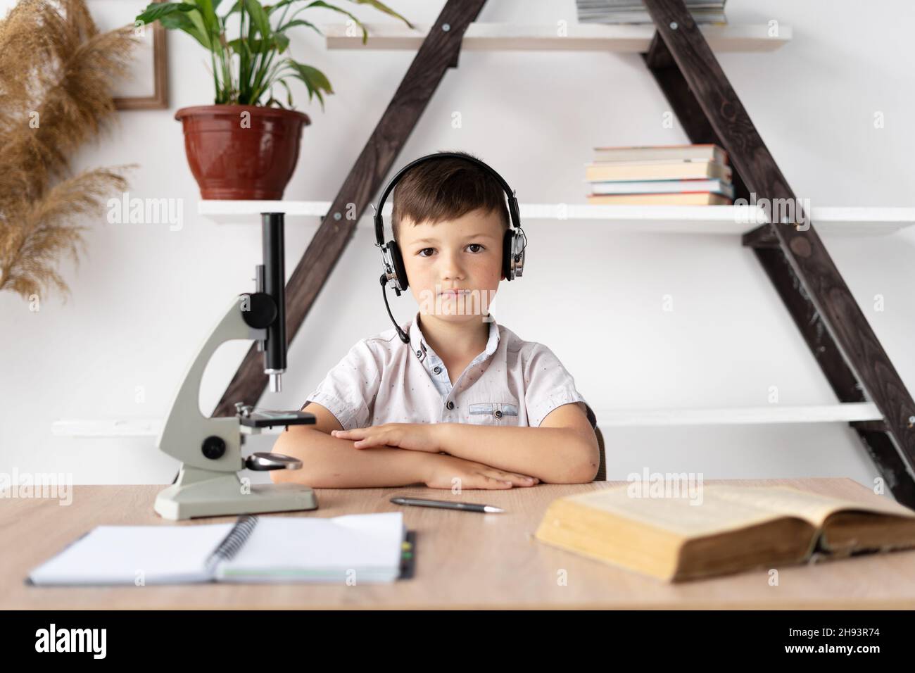 ragazzo studente in cuffie sta studiando a casa ha una lezione di biologia e un microscopio. Formazione online e insegnante di casa. Uno studente ascolta un webinar Foto Stock