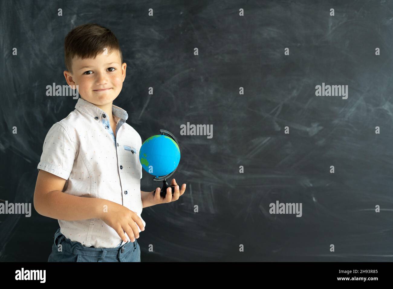 studente di scuola elementare in piedi con un globo vicino a una lavagna in una classe con una lavagna in background. Lezione di geografia per Foto Stock