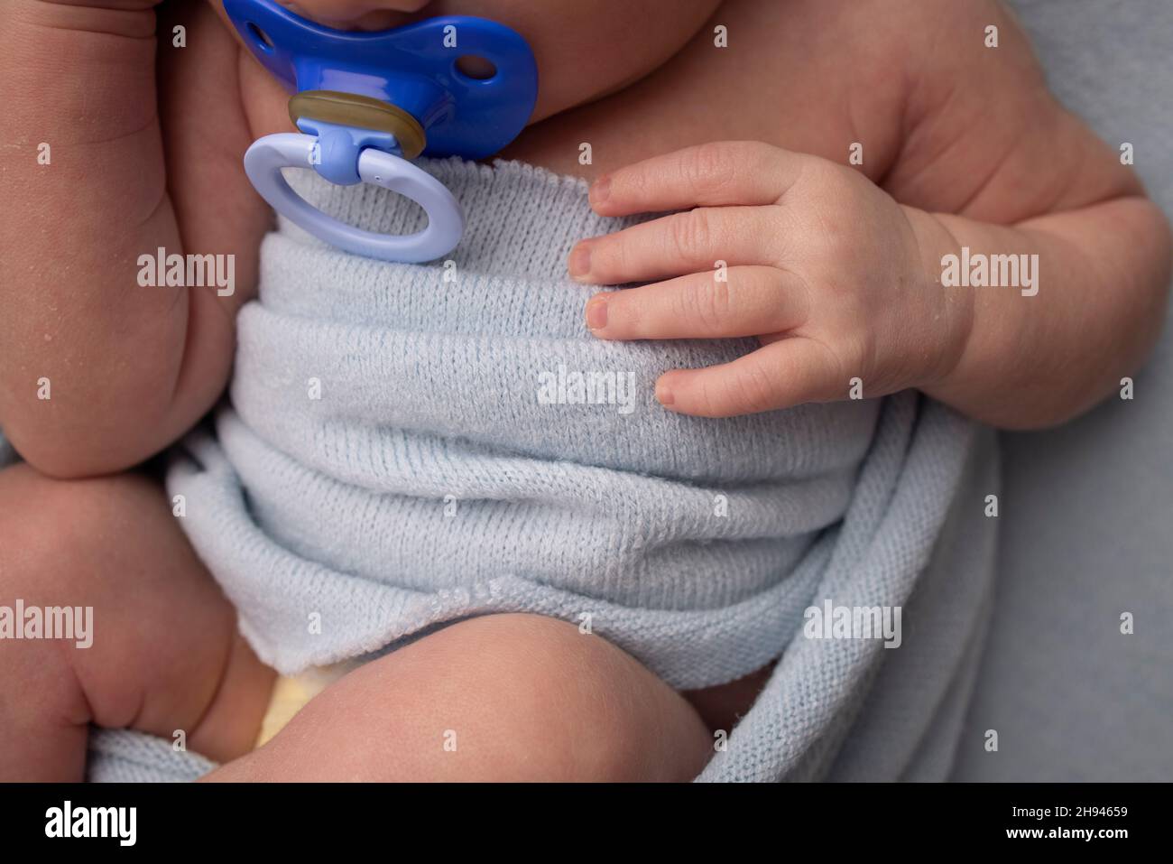 Un neonato in un avvolgimento blu dorme su sfondo blu. Mano e dita del neonato. Succhietto da primo piano succhietto fittizio. Macrofotografia studio. Foto Stock