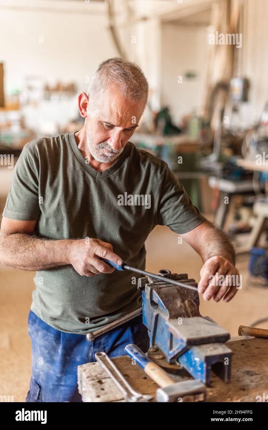Lavoratore di sesso maschile che archiva un utensile in metallo su un banco di lavoro Foto Stock