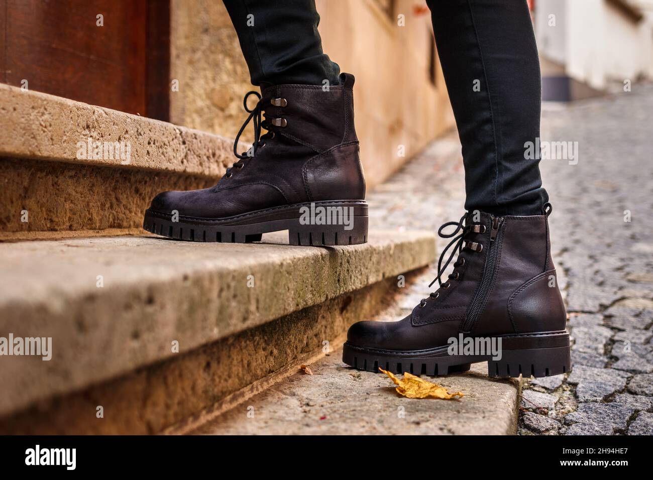 Stivali alla moda in pelle nera. Scarpe eleganti da primo piano. Gambe femminili che camminano su scala su strada Foto Stock
