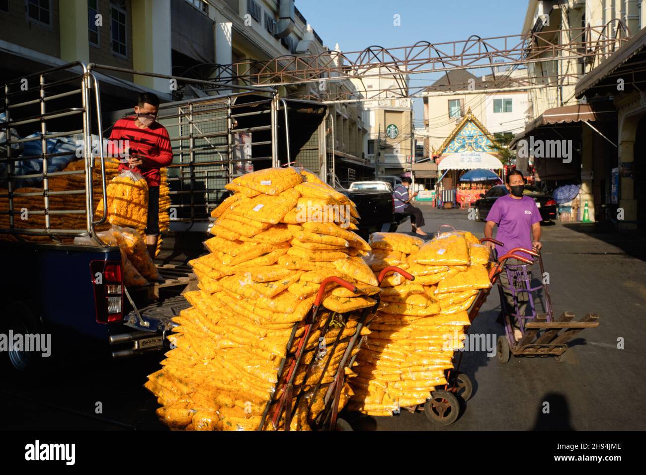 Un fattorino al mercato dei fiori di Yodpiman a Pak Klong Talaat, Bangkok, Thailandia, caricando un carrello con sacco di fiori marigold Foto Stock