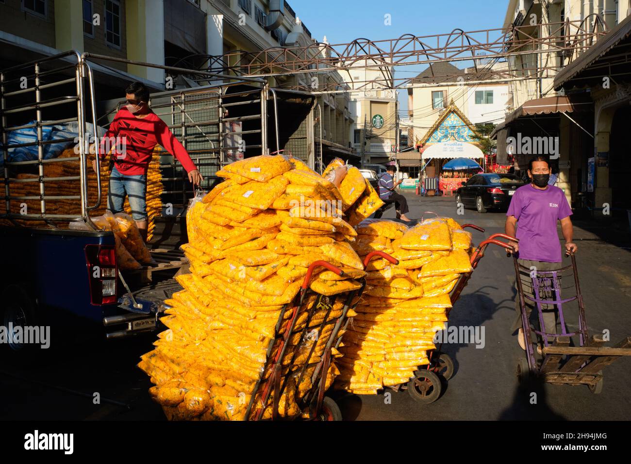 Un fattorino al mercato dei fiori di Yodpiman a Pak Klong Talaat, Bangkok, Thailandia, caricando un carrello con sacco di fiori marigold Foto Stock