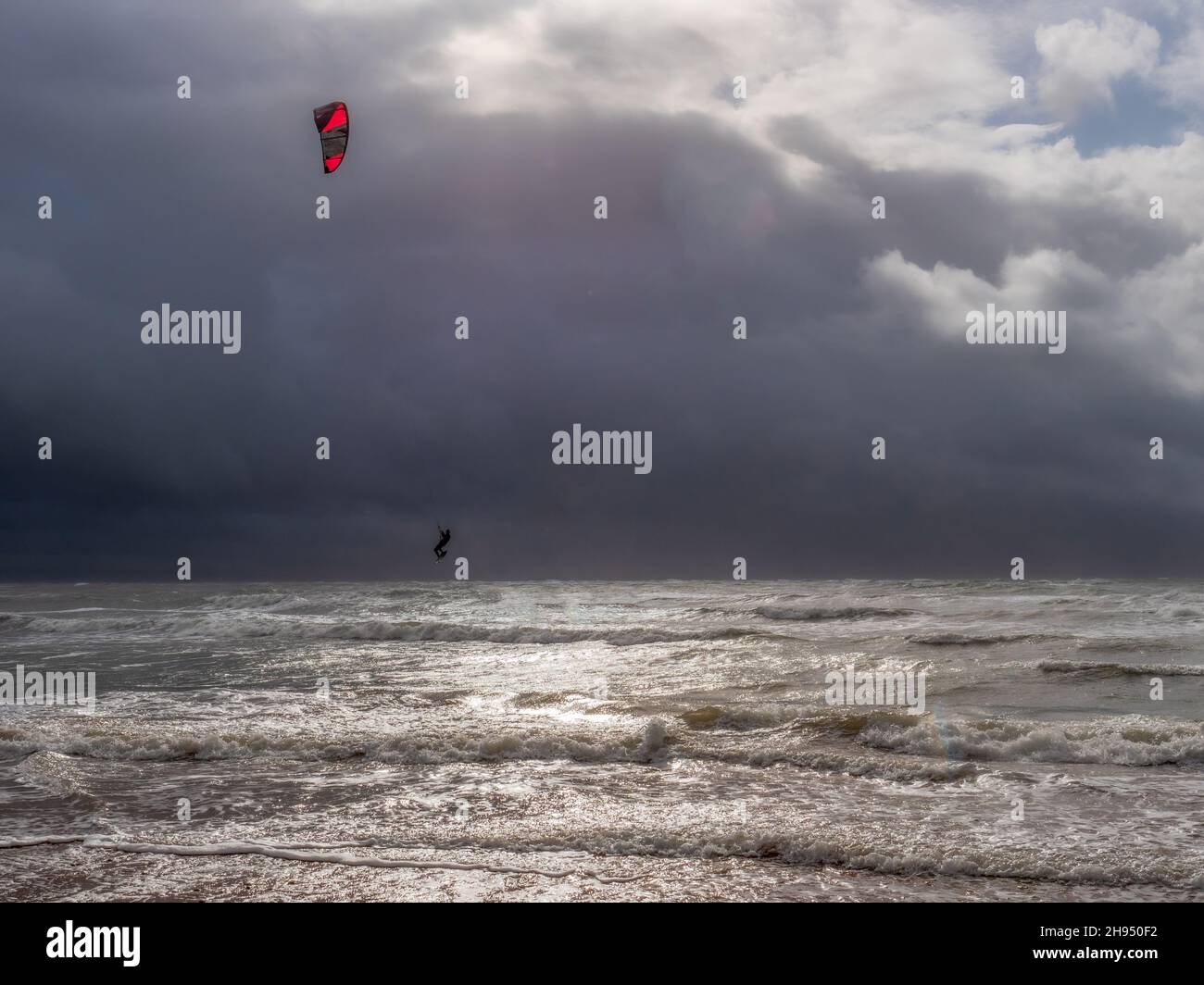 Un kitesurfer surf lungo le onde su una spiaggia di sabbia contro un cielo nuvoloso e tempestoso in Galles Foto Stock