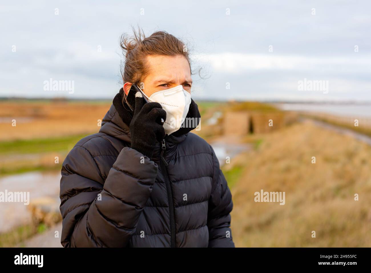 Un giovane uomo che indossa una maschera facciale KN95 One use mentre usa il suo cellulare durante la pandemia del virus della corona Covid-19 Foto Stock