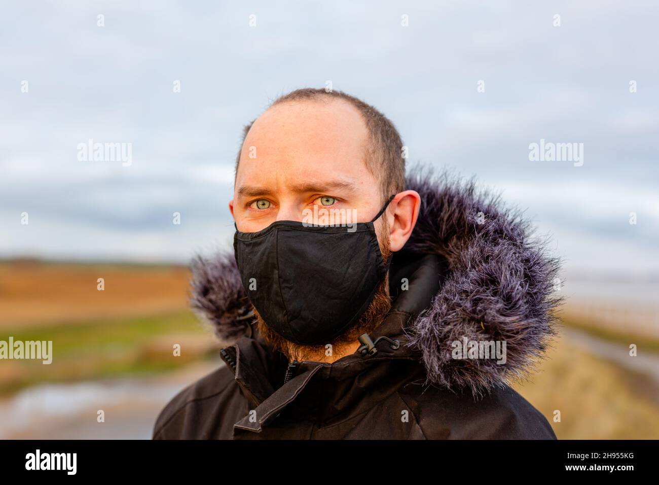 Un giovane uomo che indossa una maschera nera lavabile durante la pandemia del virus della corona di Covid-19 Foto Stock
