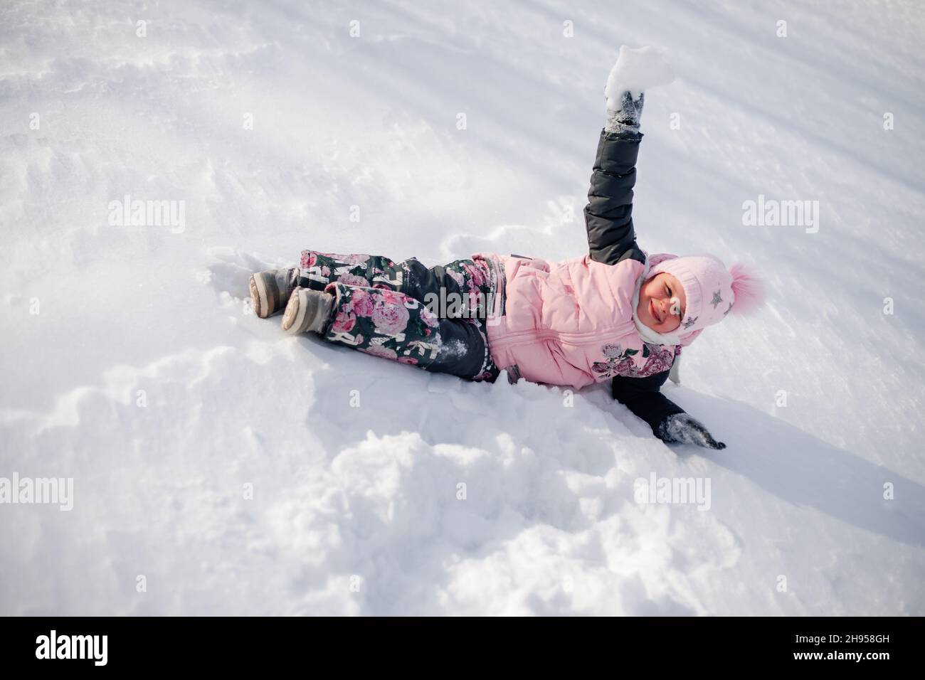 Il bambino gioca con la neve. La bambina ama passeggiare nella natura, divertirsi e cavalcare lo scivolo della neve senza slittino nella soleggiata giornata invernale Foto Stock