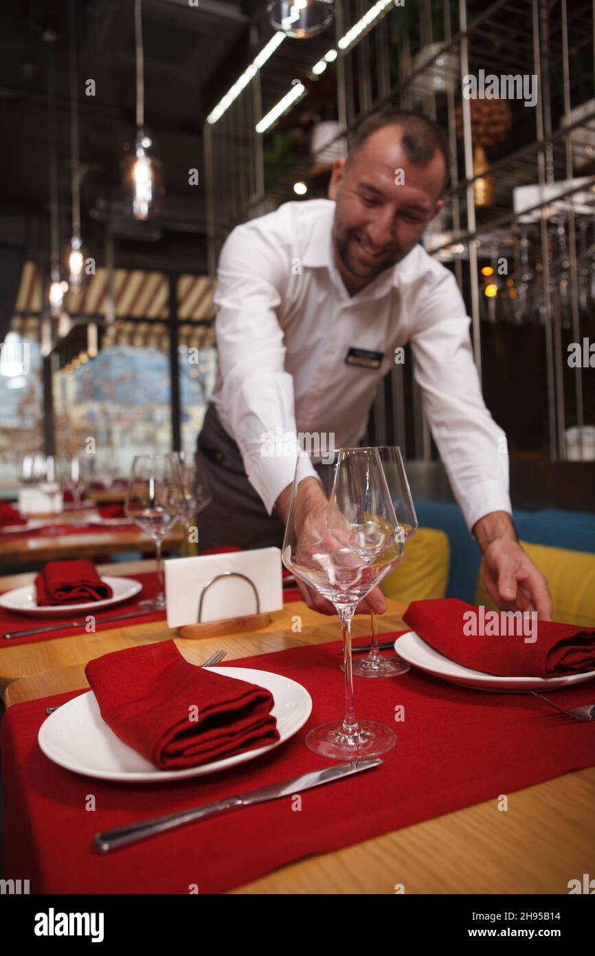 Colpo verticale di un cameriere allegro godendo di preparare tavoli per gli ospiti del ristorante Foto Stock