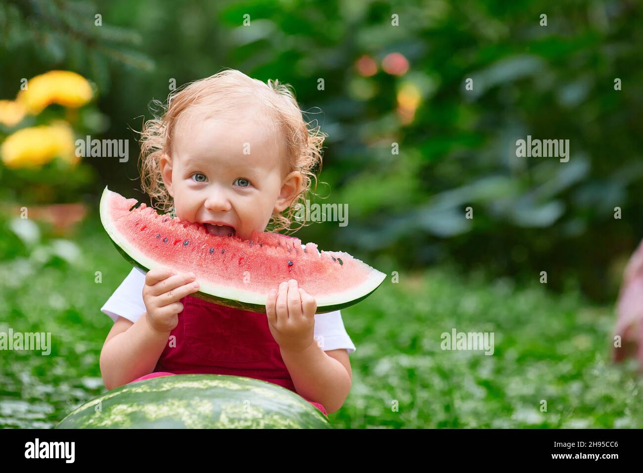 il bambino mangia un grande pezzo di cocomero per strada in una giornata estiva. Foto Stock