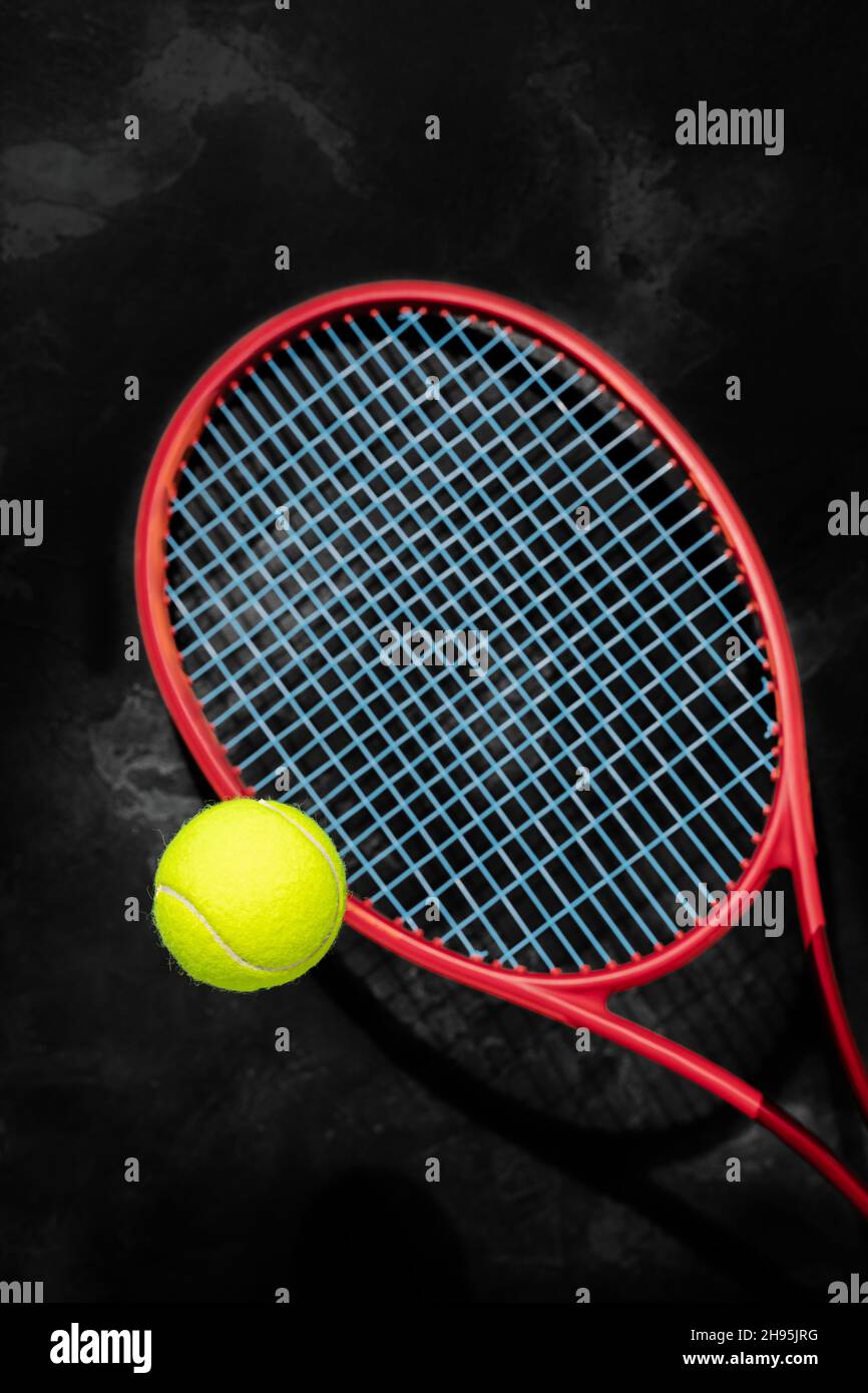 Tennis. Messa a fuoco selezionata, composizione sportiva con pallina da tennis gialla e racchetta rossa su sfondo nero testurizzato. Il concetto di gare di tennis Foto Stock
