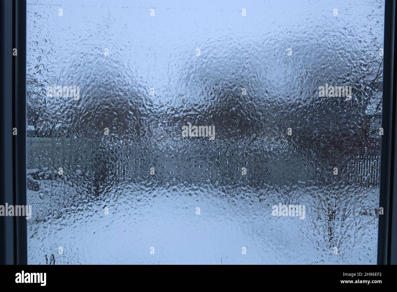 Vista attraverso una finestra coperta da uno strato di ghiaccio. Gocce di pioggia congelate sul riquadro della finestra. Foto Stock