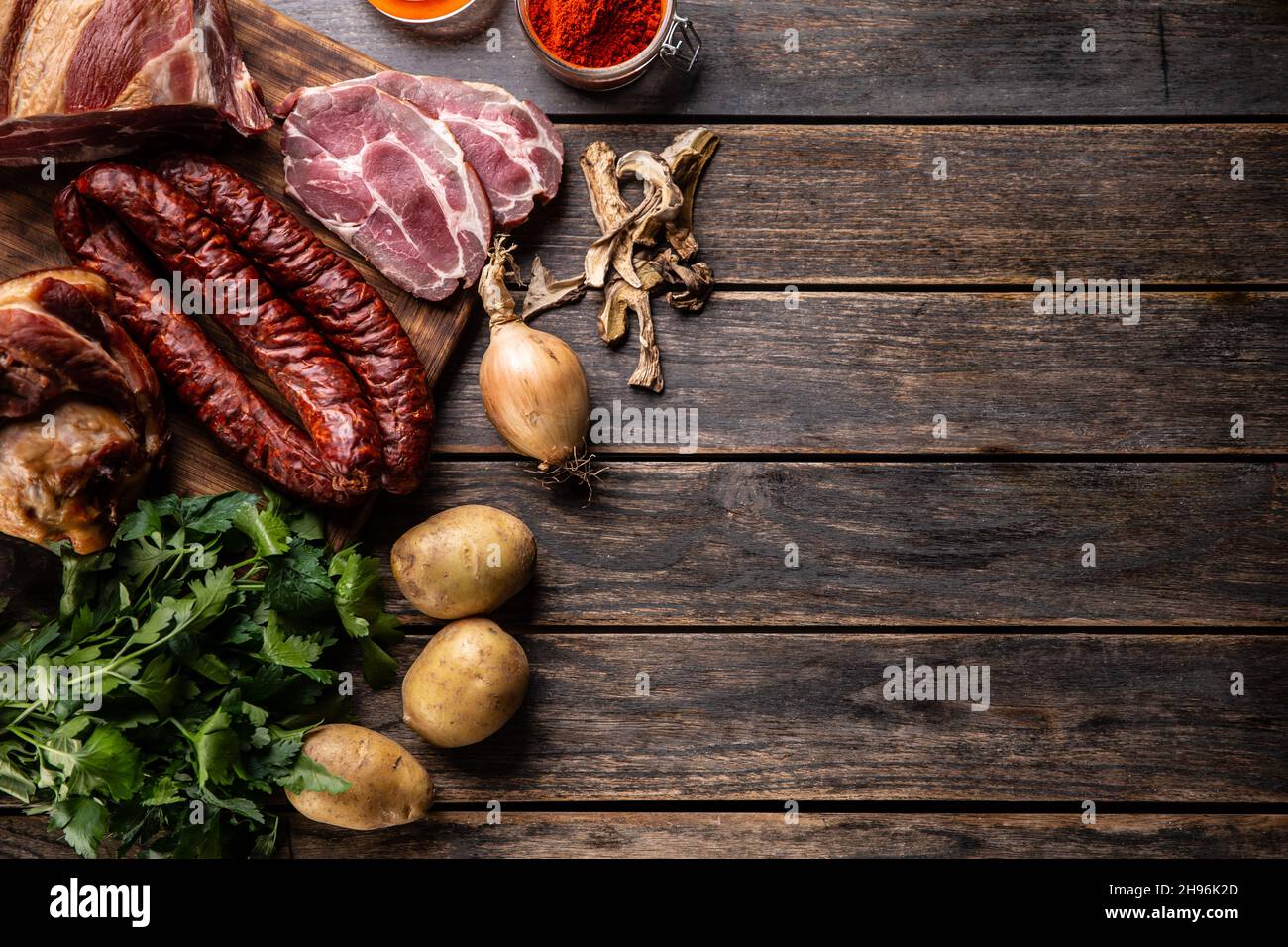 Prelibatezze malsane affumicate: Salsicce, ginocchio e collo di maiale con patate, funghi secchi con cipolla, pepe rosso macinato ed erbe aromatiche - Top of view. Foto Stock