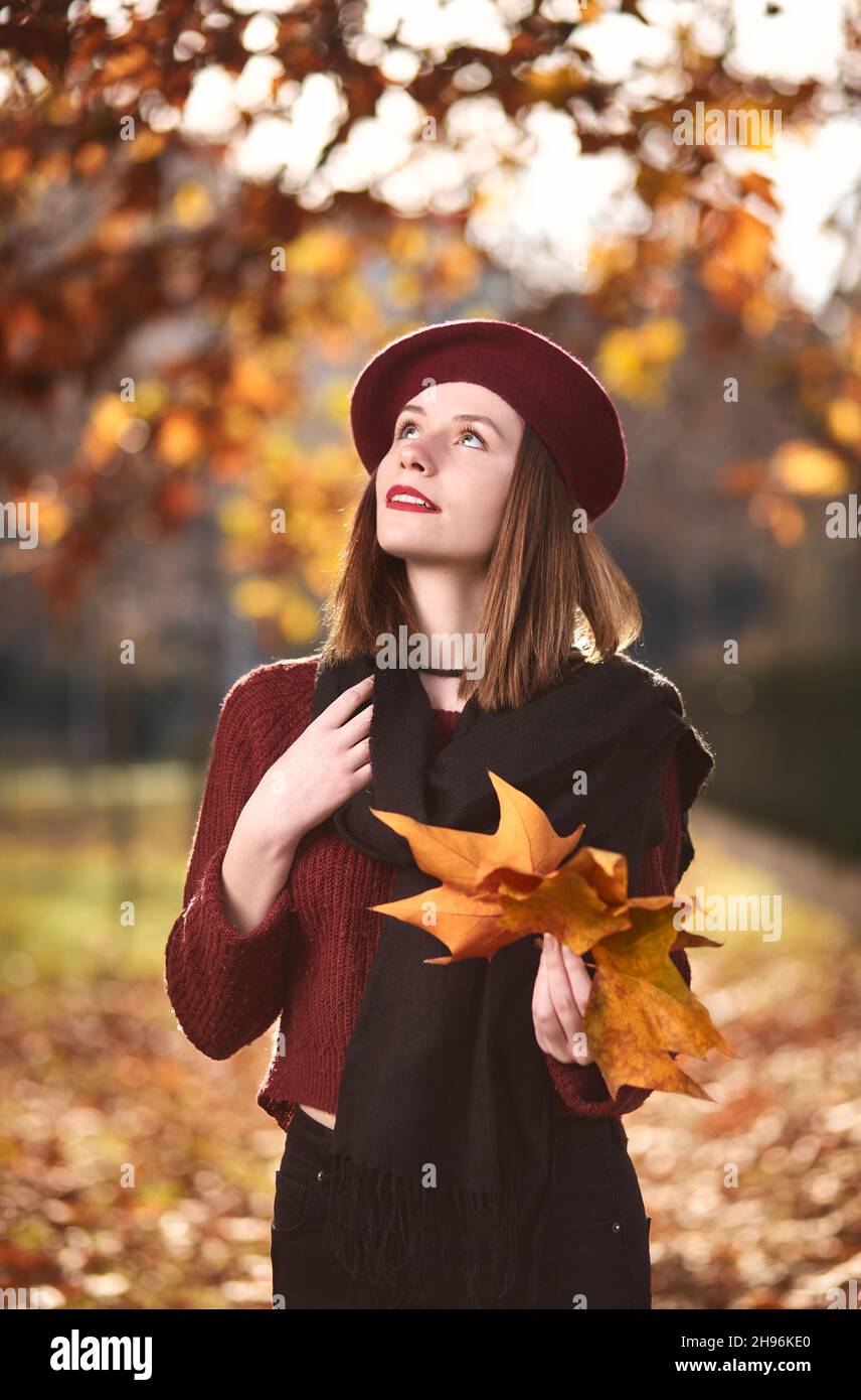 Giovane bella giornata ragazza sognando in un parco mentre tiene le foglie di acero giallo. Alberi gialli e foglie durante la stagione autunnale sullo sfondo Foto Stock