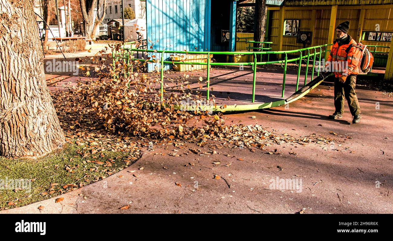 Dnepropetrovsk, Ucraina - 11.25.2021: Pulizia di foglie secche con un mulino a vento. Un lavoratore municipale pulisce il parco cittadino. Preparazione dei parchi cittadini per l'inverno Foto Stock
