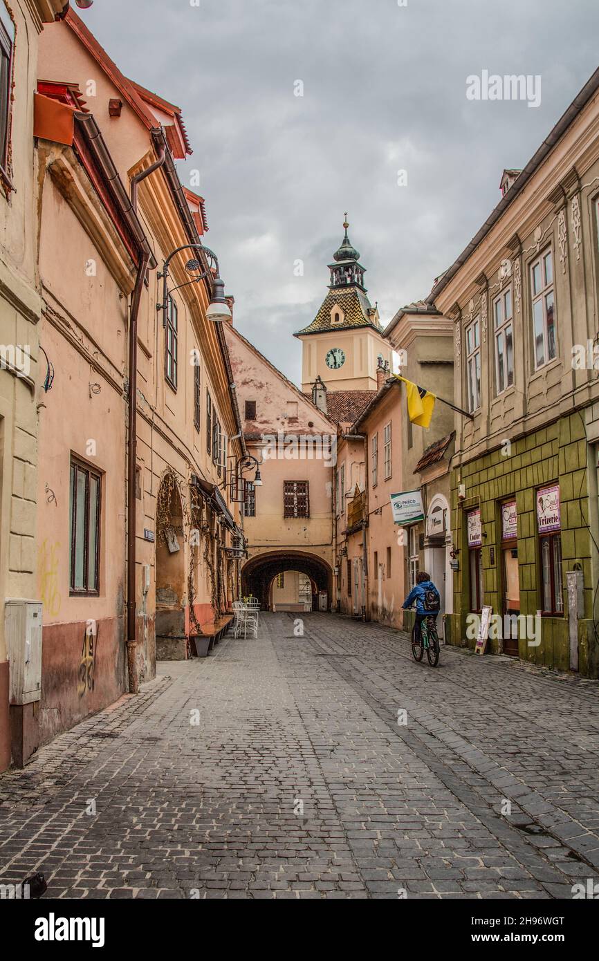 Un ciclista che scende lungo la strada di pietra di ciottoli/vicolo con un arco che porta a Piazza del Consiglio/brasov piazza principale (Piața Sfatului) in Brasov Romania. Foto Stock