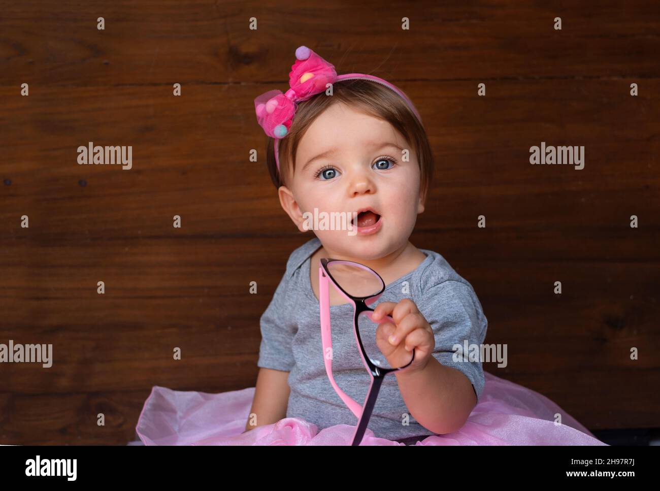 Bambino in un abito rosa su sfondo di legno. Bambino carino con arco Foto Stock