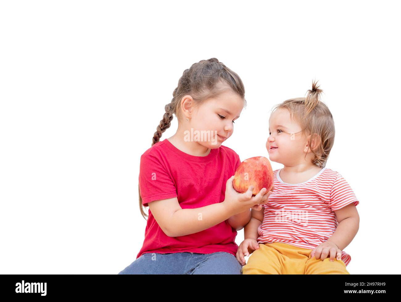 Due bambini condividono una mela. Una ragazza tiene fuori una mela alla sua sorella più giovane. Foto Stock