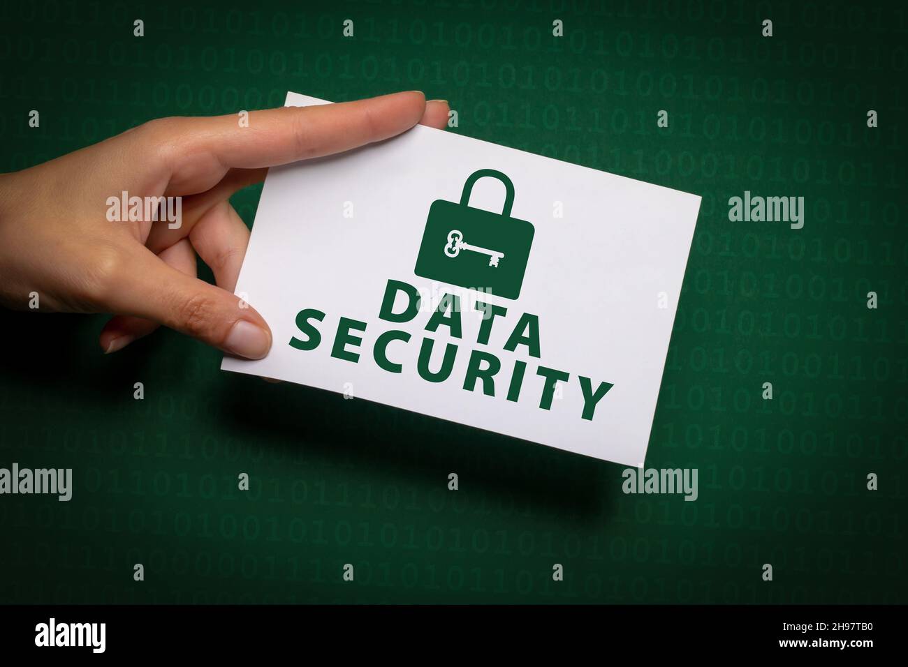 La mano femmina contiene un pezzo di carta con l'iscrizione Data Security e il simbolo di blocco in verde scritto su sfondo verde scuro con codice binario Foto Stock
