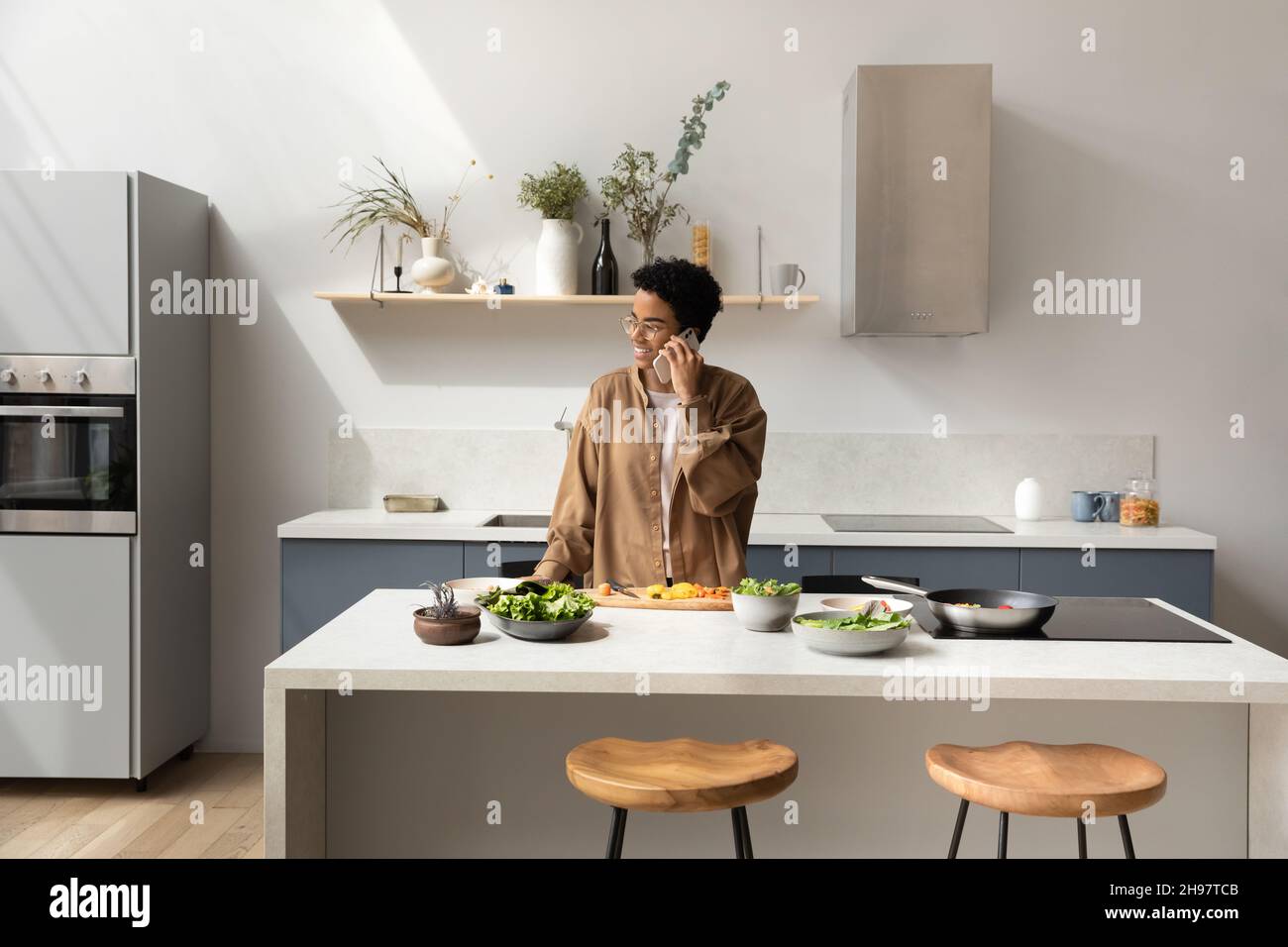 Felice giovane afroamericana che parla, cucinando in cucina. Foto Stock