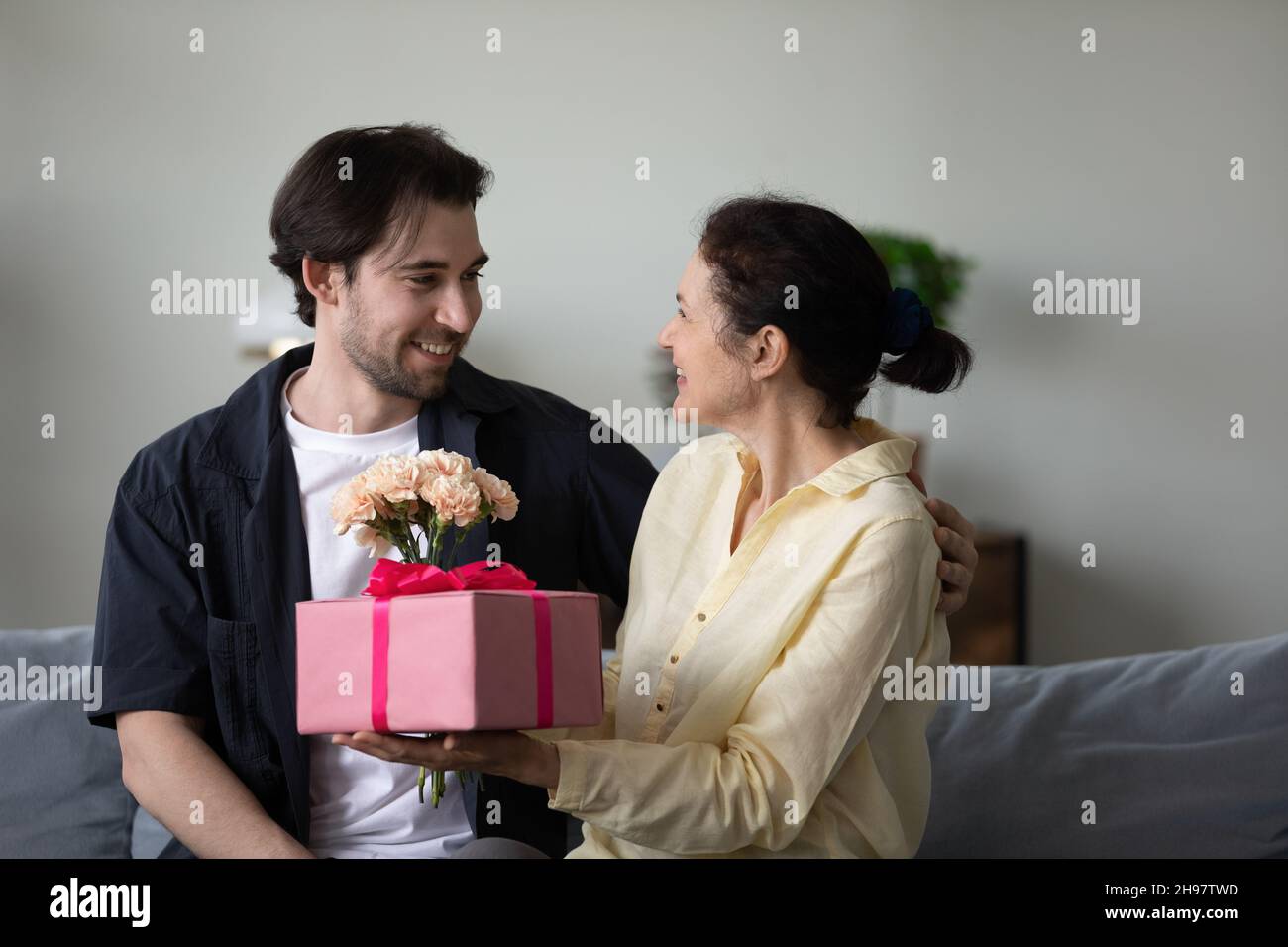 Mamma di mezza età eccitata che riceve un regalo a sorpresa e un mazzo di fiori Foto Stock