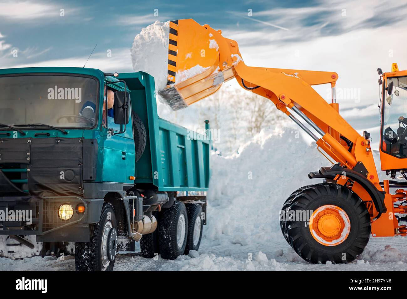 Rimozione della neve dopo la nevicata e le bizzard. L'escavatore carica la neve nel dumper. Lavori di servizi di pubblica utilità durante l'inverno di periodo Foto Stock