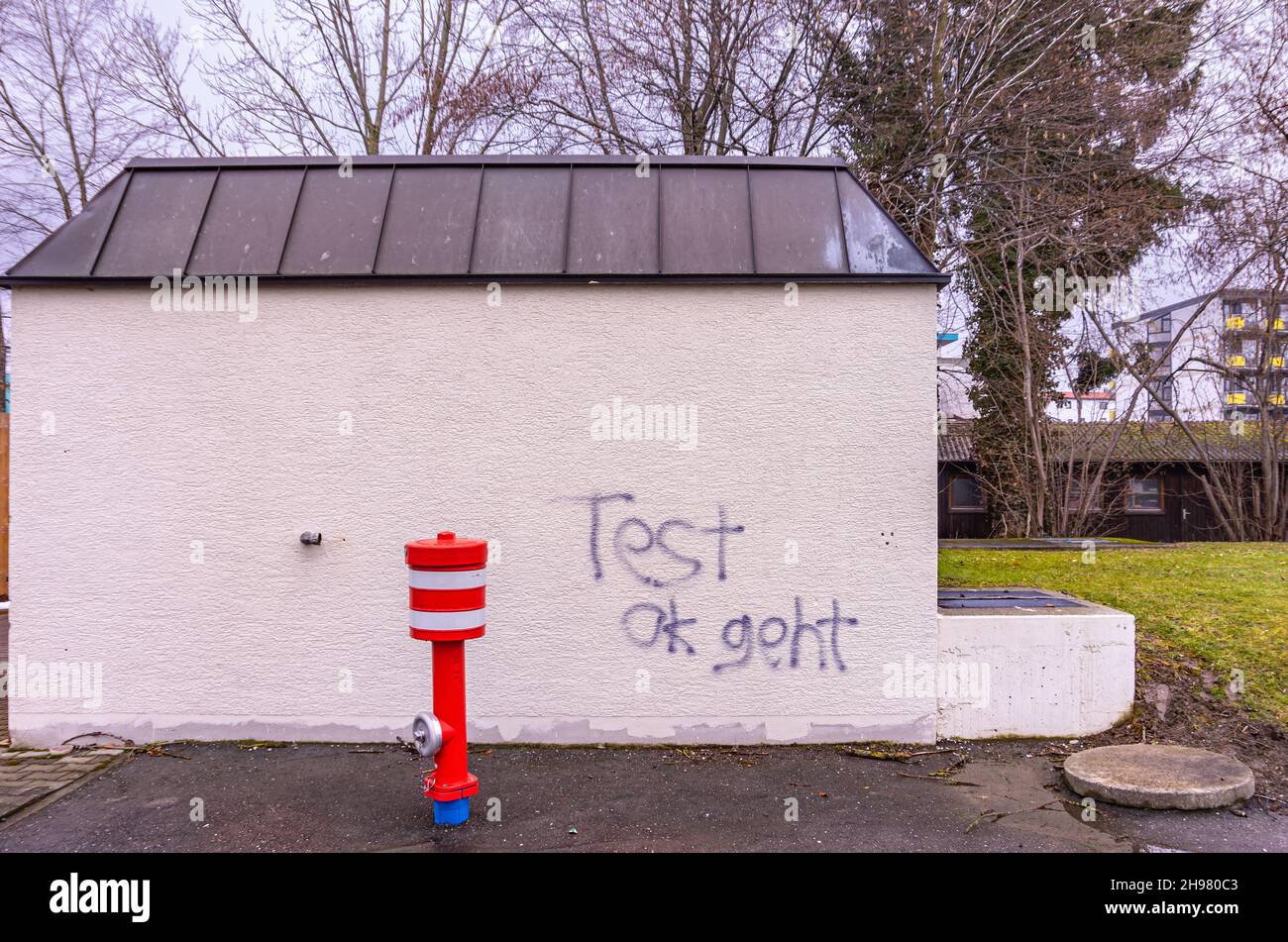 Idrante di fronte a un edificio bianco coperto di graffiti con le parole tedesche "Test ok geht". Foto Stock