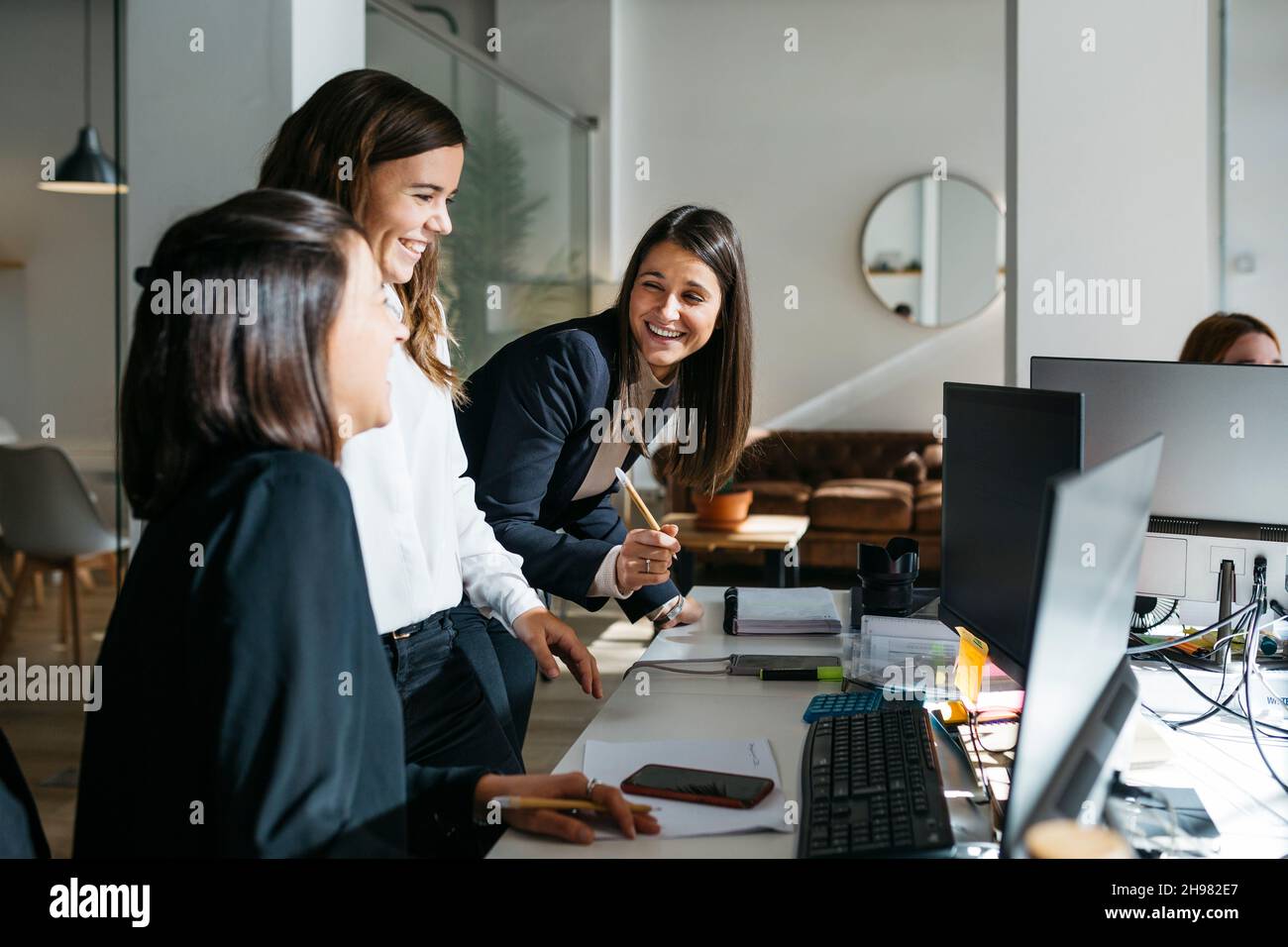 Tre donne d'affari sorridenti che parlano di lavoro davanti a un computer in ufficio. Sono in astuti casuals. Foto Stock