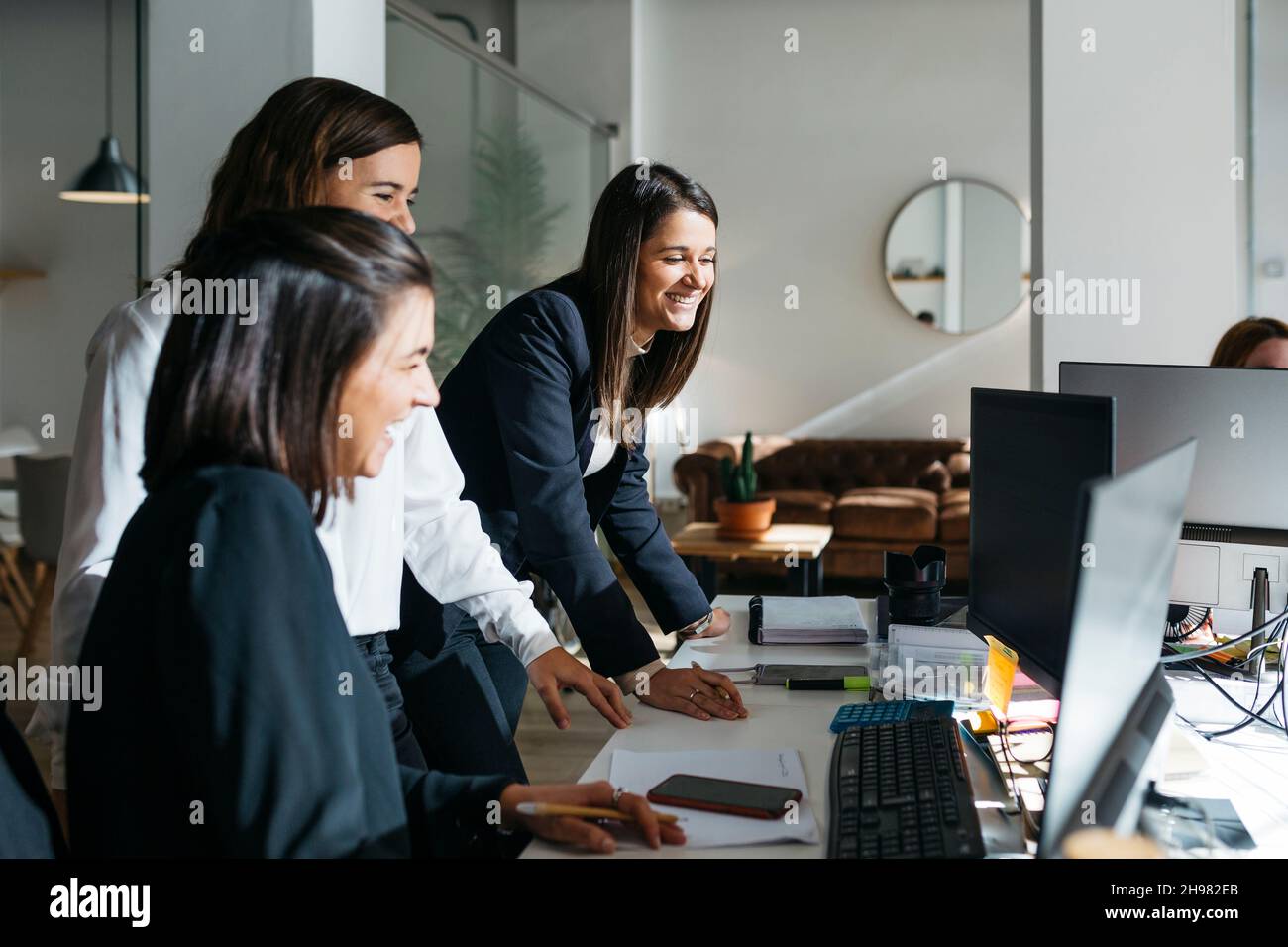 Tre donne d'affari sorridenti che parlano di lavoro davanti a un computer in ufficio. Sono in astuti casuals. Foto Stock